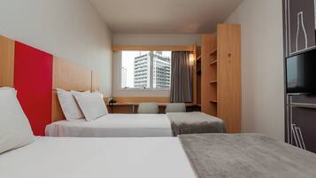 A hotel room with two beds, a TV, a desk, and a window with a city view.