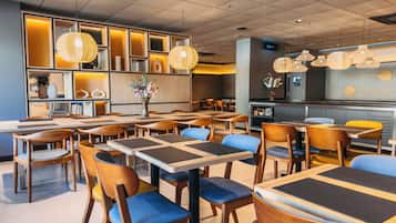 Un restaurante moderno con mesas y sillas de madera, un arreglo floral central y lámparas colgantes de mimbre.