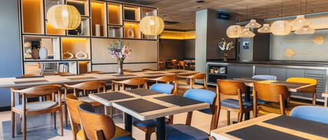 A modern restaurant with wooden tables and chairs, a central floral arrangement, and hanging wicker lamps.