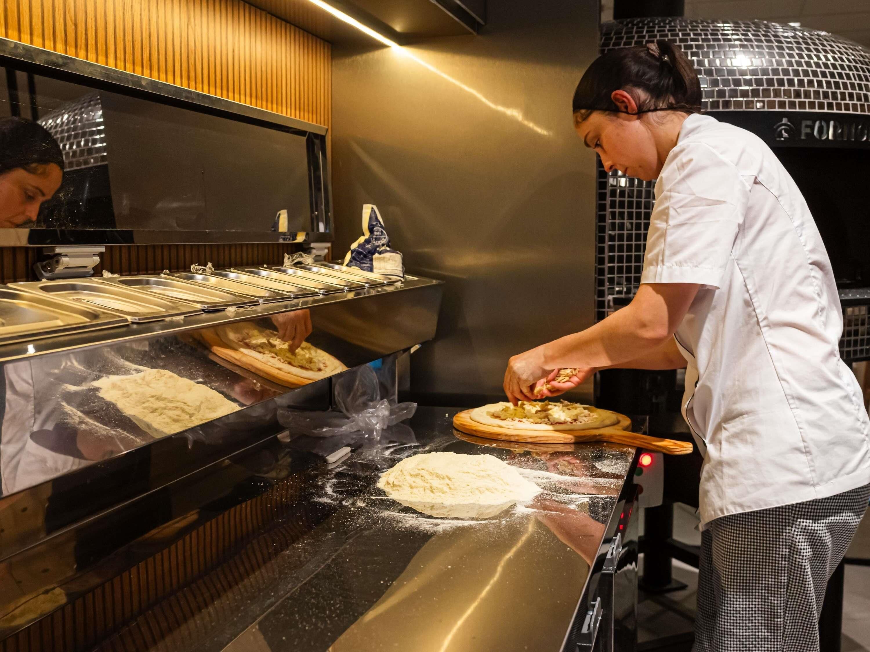 Una cocina con una persona preparando comida, una encimera de acero inoxidable y un horno de pizza al fondo.
