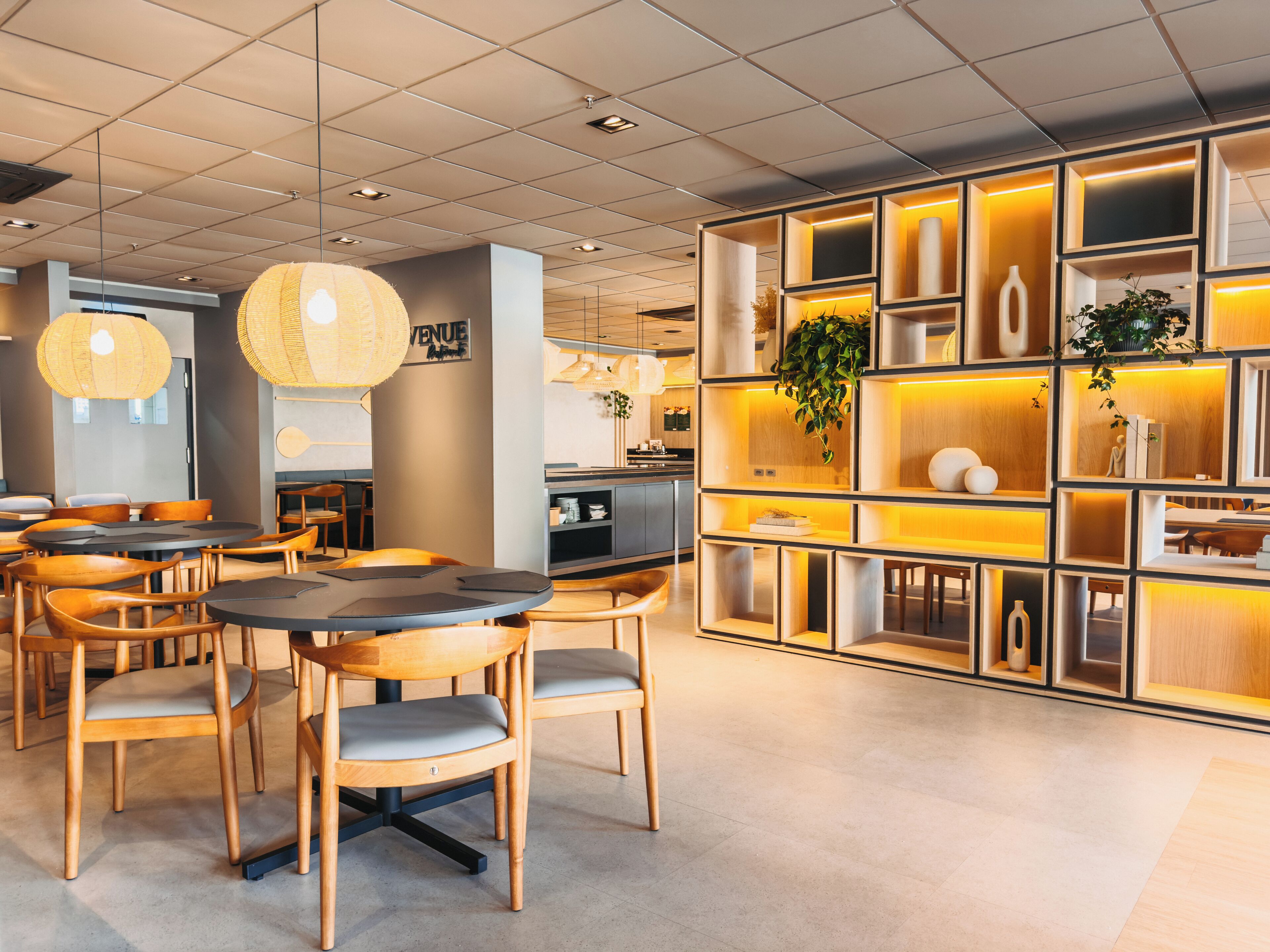 A modern restaurant interior with round tables, wooden chairs, and a decorative wall with shelves.