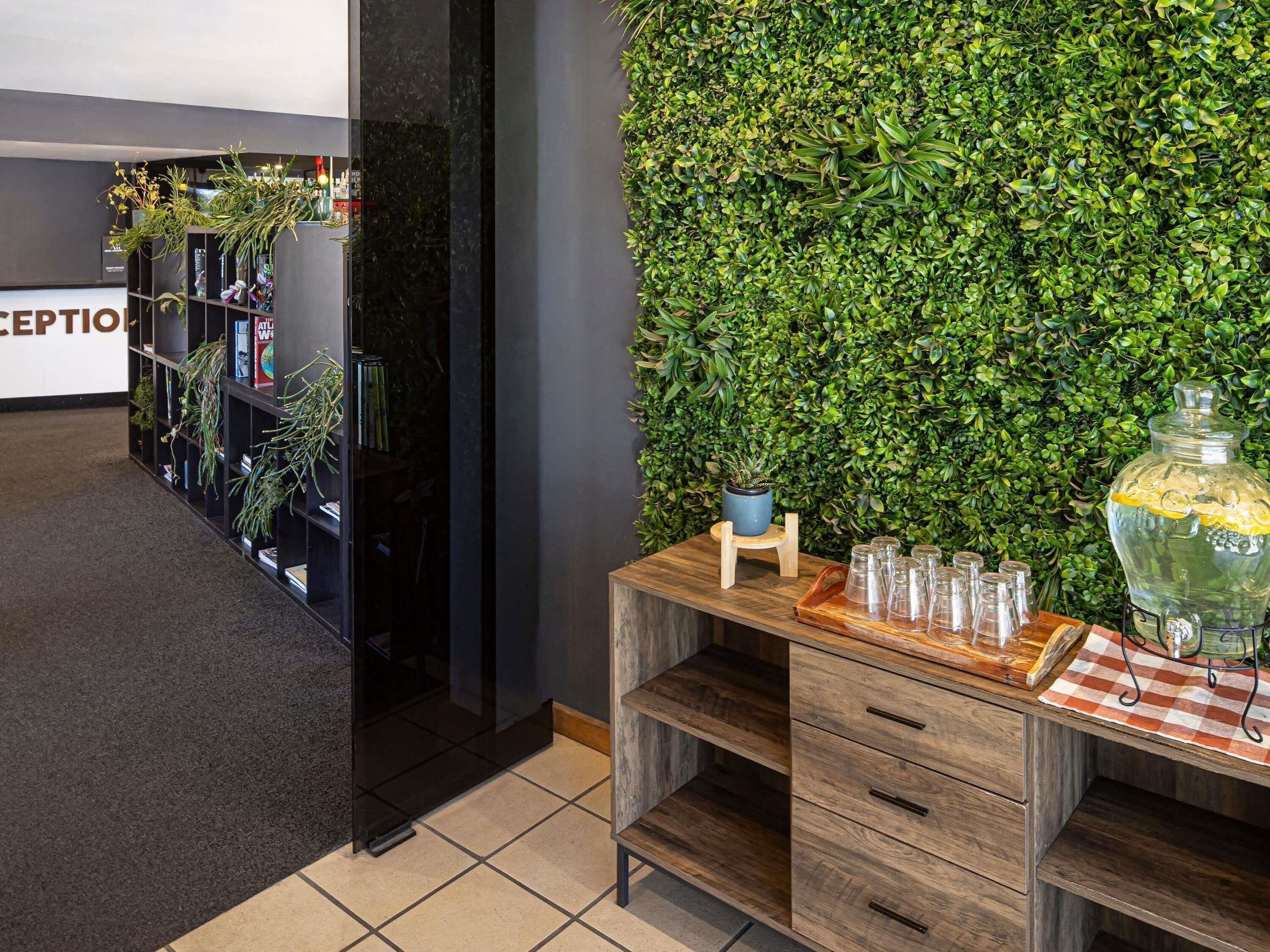 Een receptiegedeelte met een groene wand, een houten toonbank met glazen en een boekenkast met planten.