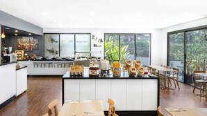 Una cocina moderna con una isla central, comedor con sillas de madera y grandes ventanales con vistas a la vegetación.
