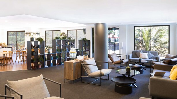 Una sala de estar moderna con un sofá, sillones y una mesa de centro. Hay libros y un jarrón sobre la mesa de centro.