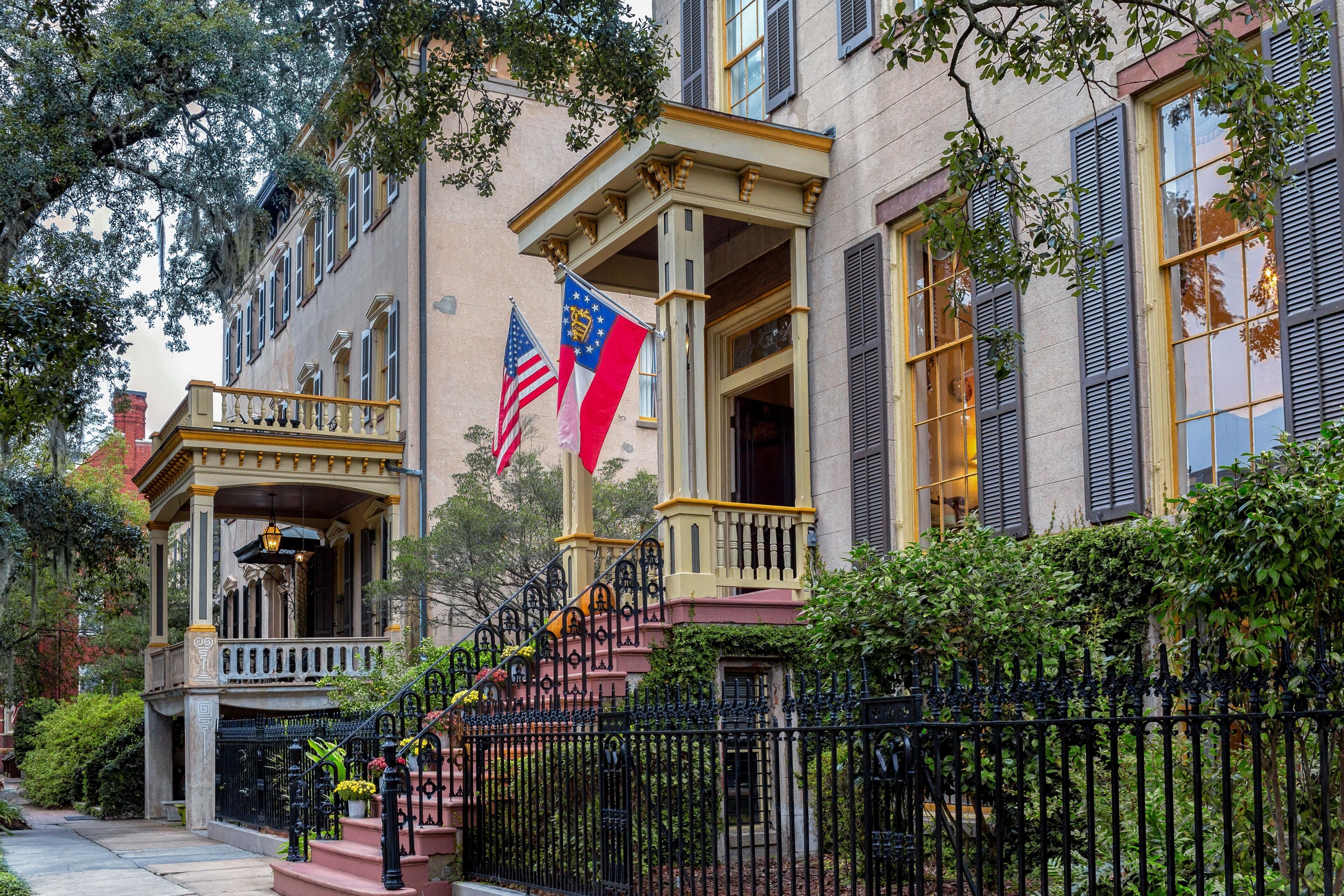 A historic building with a prominent entrance, two flags, and a black wrought iron fence.