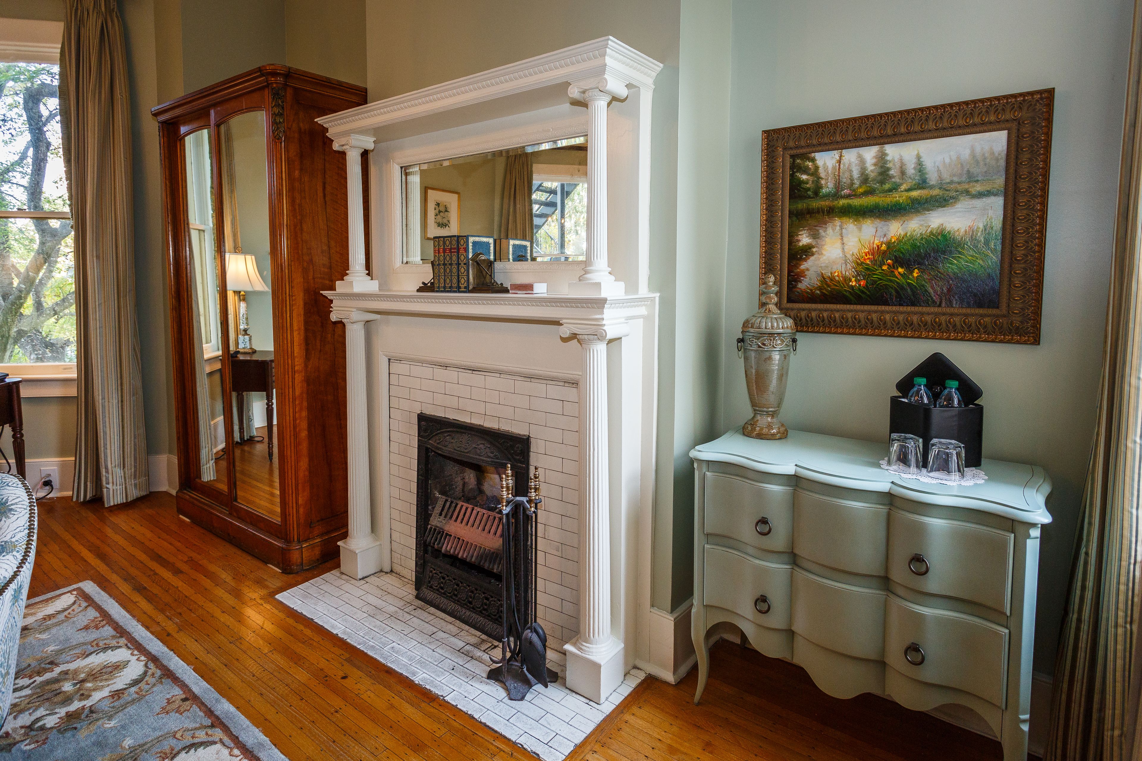 A room with a fireplace, a mirror, a dresser, and a painting on the wall.