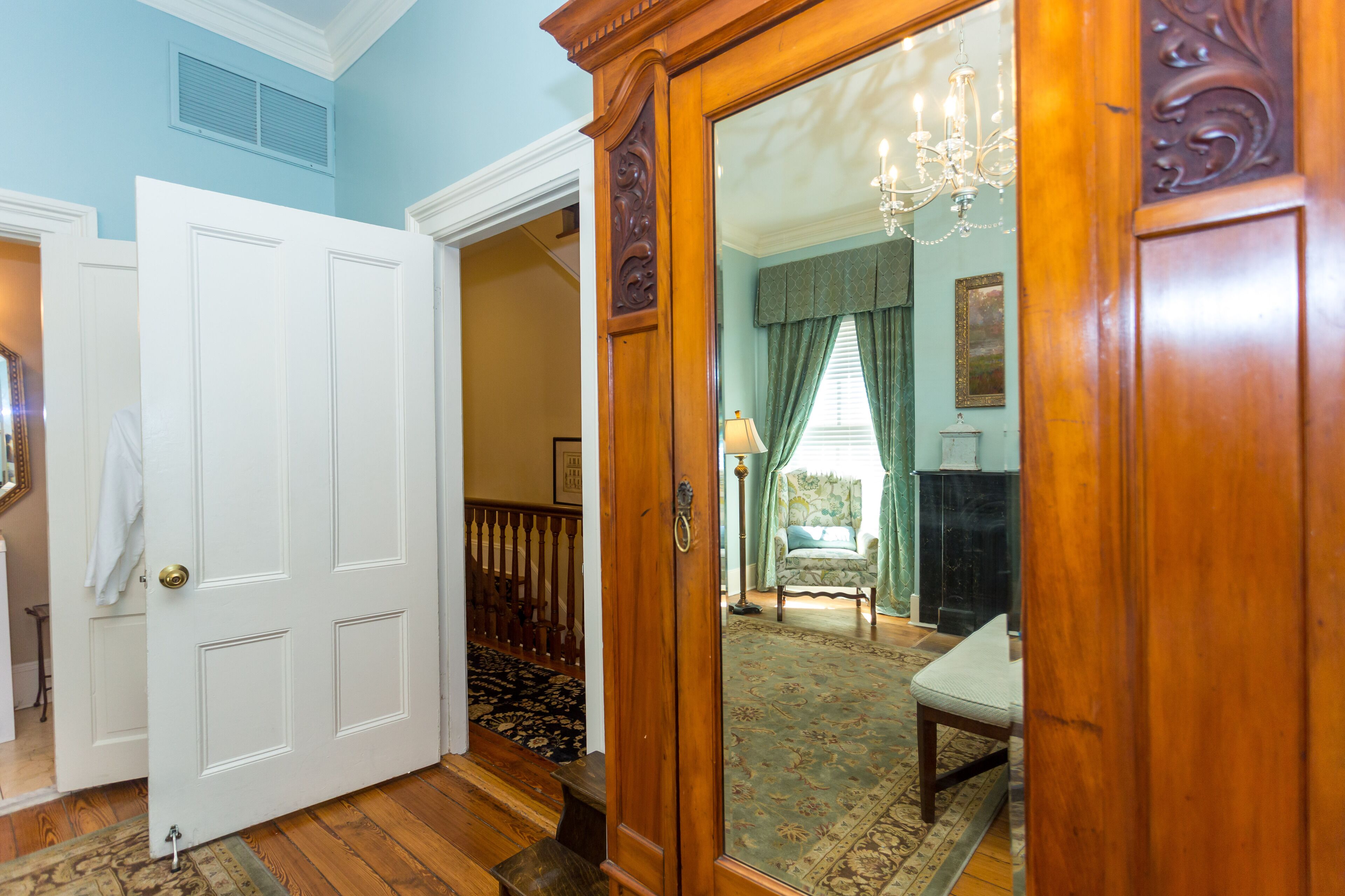 A room with a wooden door, a mirror, a chandelier, a patterned rug, and a green upholstered chair.