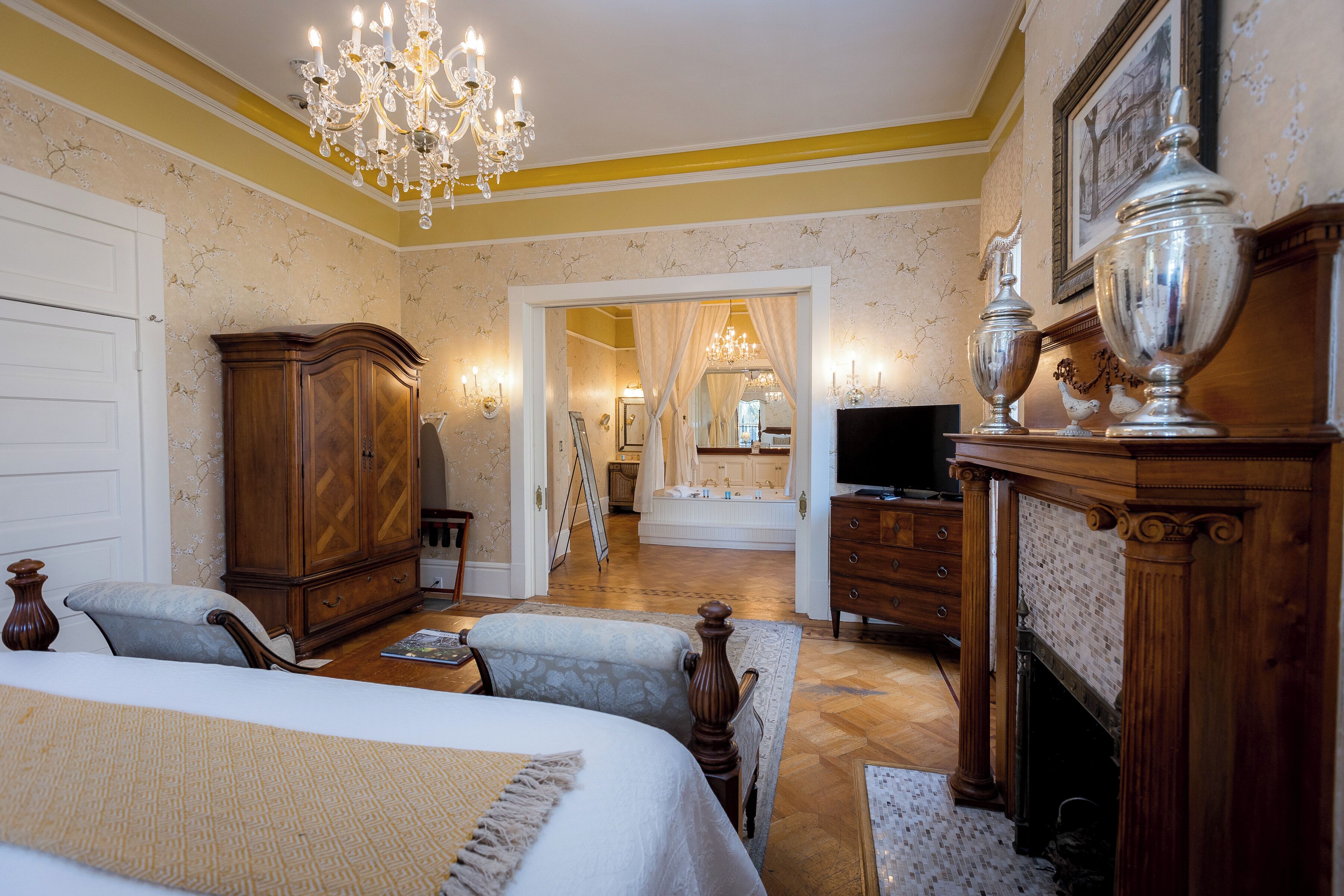 A bedroom with a large bed, a wooden wardrobe, a television, and a fireplace.