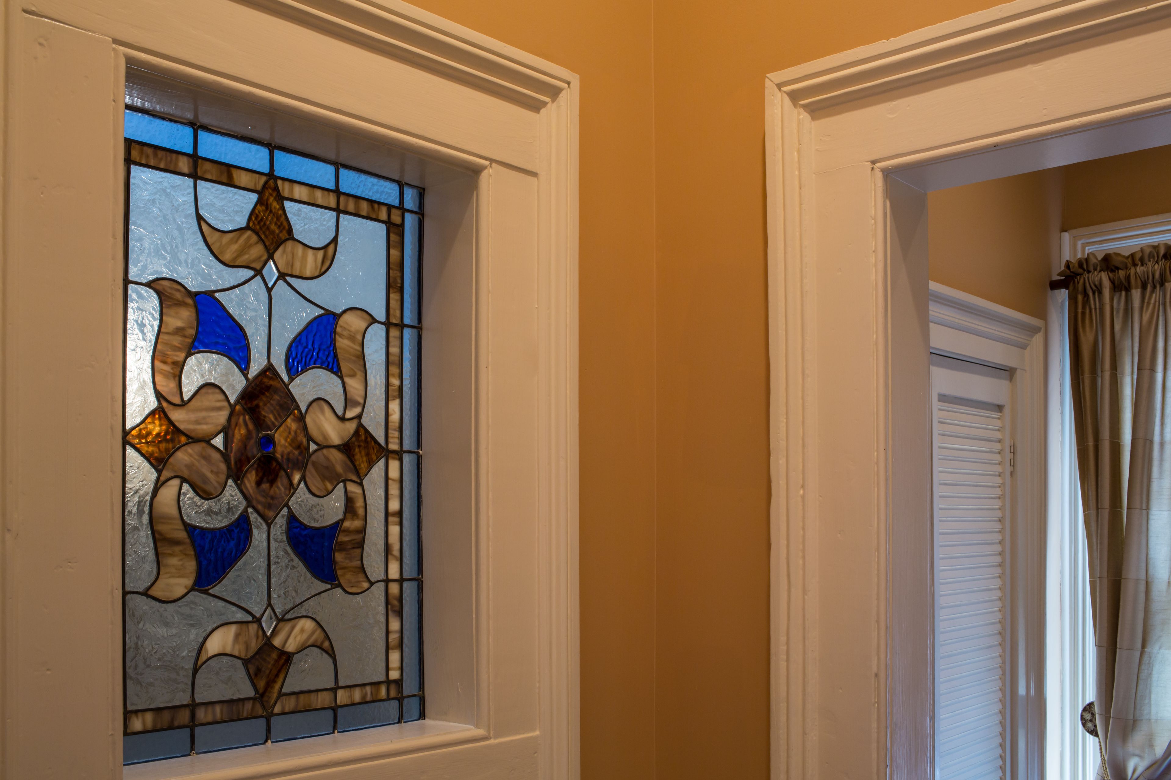 A stained glass window with a geometric design, a white door with a shutter, and beige walls.