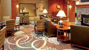 A hotel lobby with striped armchairs, a sofa, a fireplace, and a clock on the wall. - Aspen Suites (Rochester)