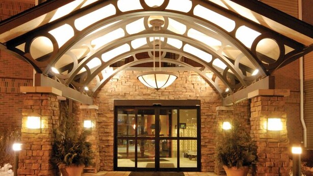 A hotel entrance with a stone facade, a glass door, and a metal roof structure. - Aspen Suites (Rochester)