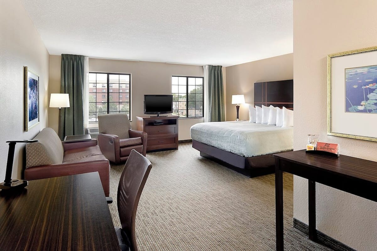 A hotel room with a bed, a desk, a chair, a TV, and a window with curtains.