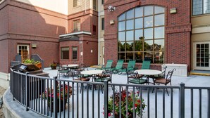 An outdoor patio area with brick walls, a large arched window, and outdoor seating. - Aspen Suites (Rochester)