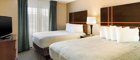 Habitación de hotel con dos camas, televisión, lámpara y vistas al exterior.