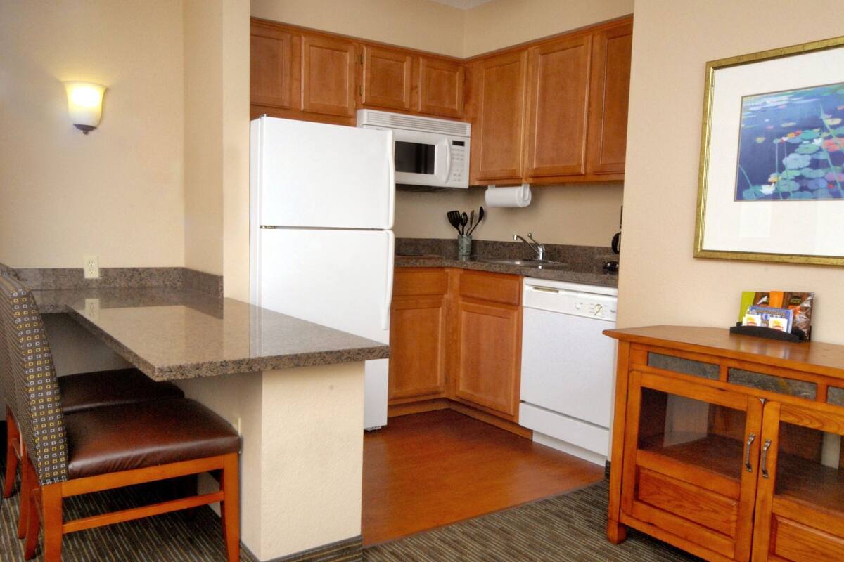 A compact kitchen with wooden cabinets, a white refrigerator, a microwave, and a dishwasher.