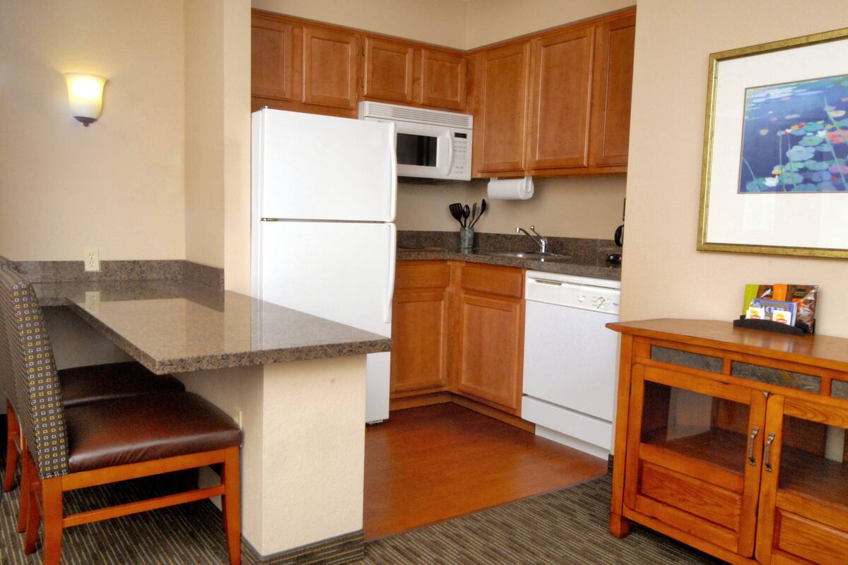 A kitchen with wooden cabinets, a white refrigerator, a microwave, a dishwasher, and a granite countertop.