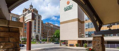 A hotel entrance with a prominent Aspen sign, a large brick building in the background, and a clear sky.