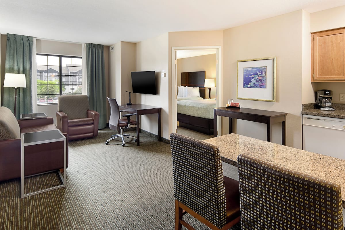 A hotel room with a bed, desk, chair, TV, and kitchenette.