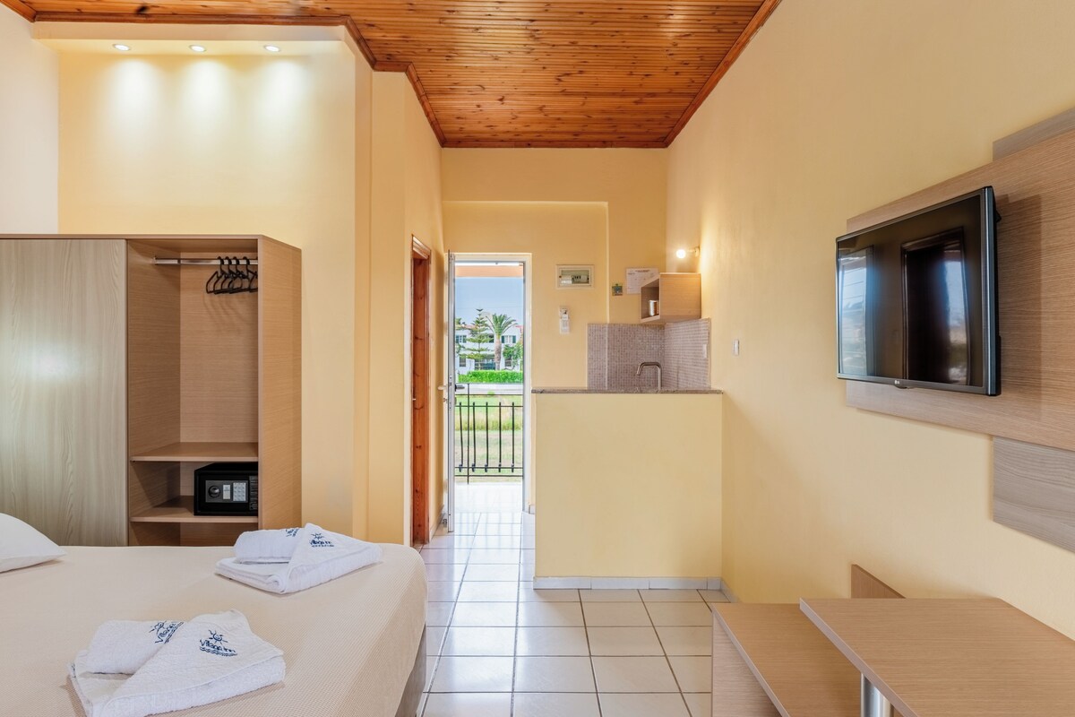A hotel room with a bed, a wooden wardrobe, a TV mounted on the wall, and a small kitchenette.