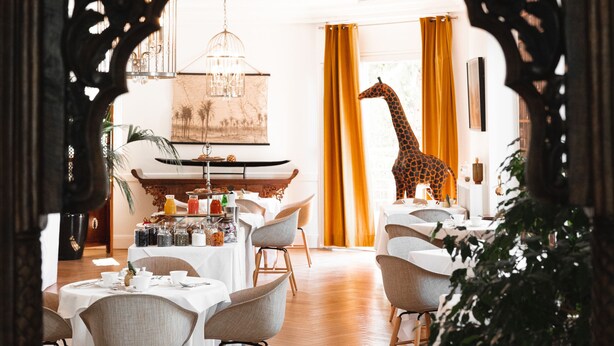 An interior dining area with a wooden archway, a giraffe sculpture, and a table set for a meal.