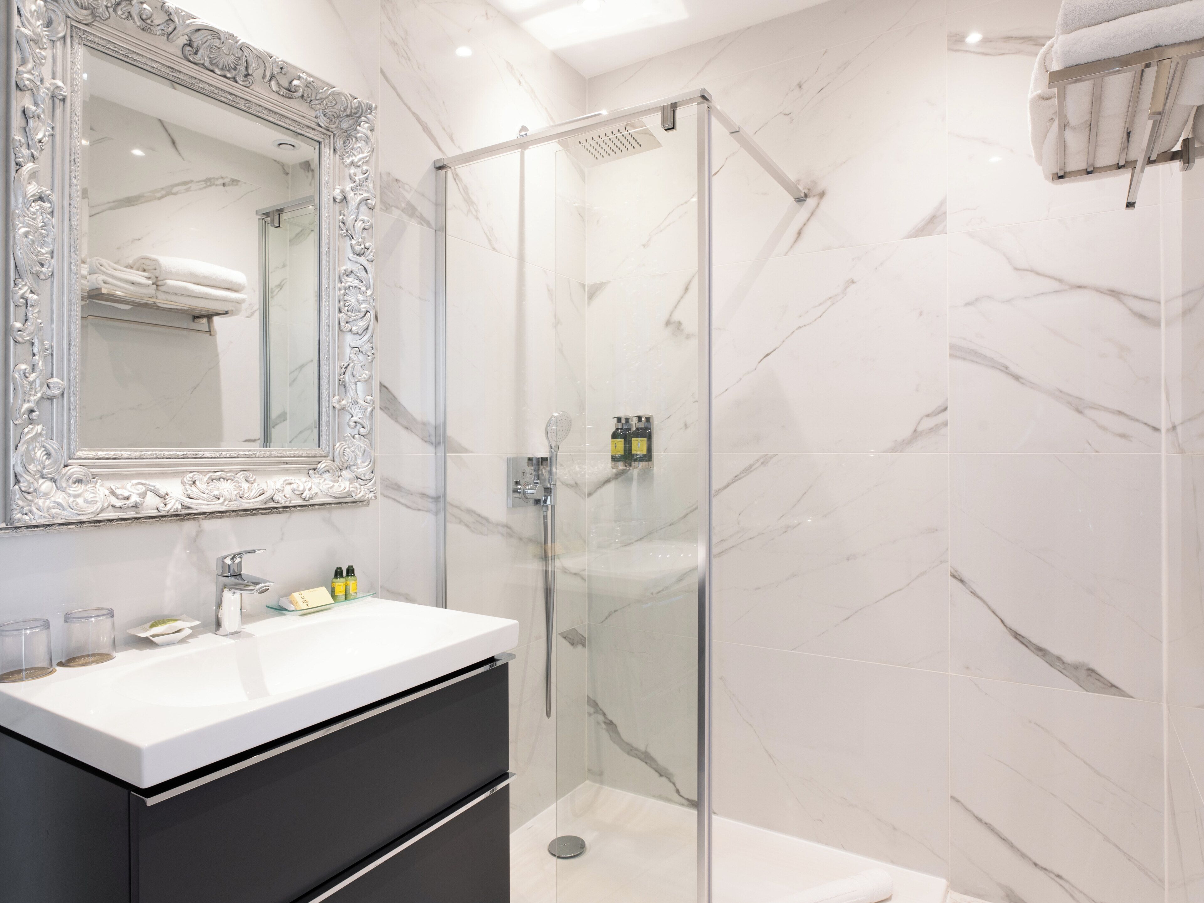A modern bathroom with a glass-enclosed shower, a white marble wall, and a large ornate mirror.