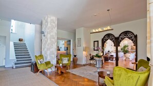 A spacious living area with a herringbone wood floor, green armchairs, a coffee table, and a staircase leading to an upper level.