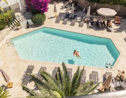 A swimming pool with lounge chairs and umbrellas, surrounded by potted plants and a stone wall.