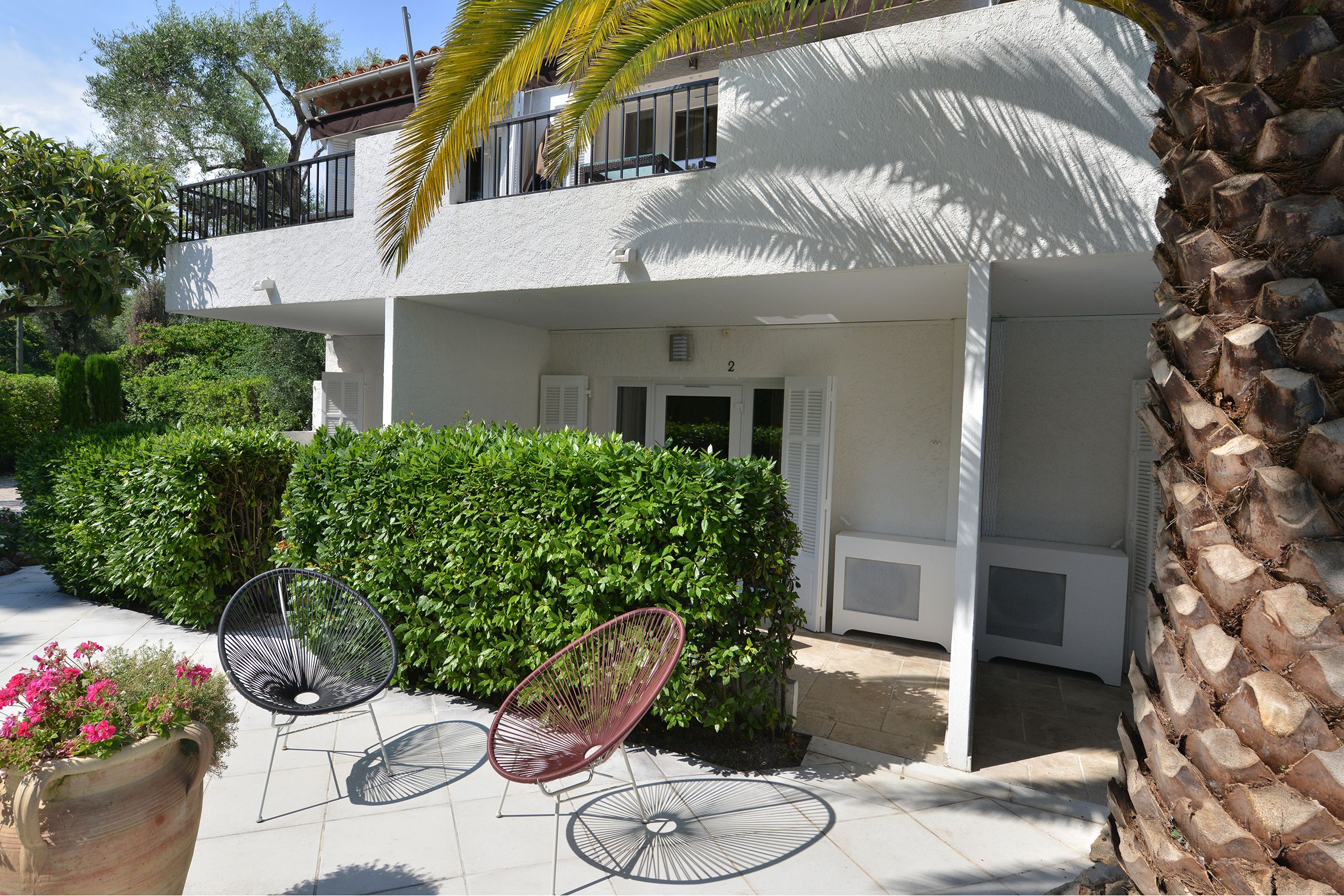 A two-story building with a balcony, a covered patio area, and a large potted plant.