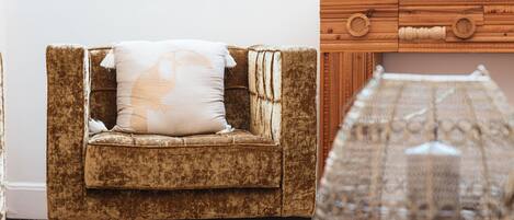Un sillón marrón con un cojín blanco, un aparador de madera con pomos redondos y una alfombra estampada.