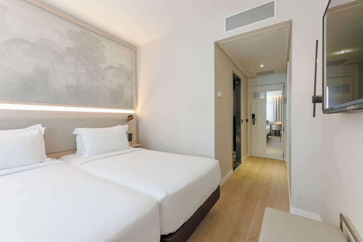 Habitación de hotel con dos camas, un cuadro grande en la pared, un espejo y vistas al baño.