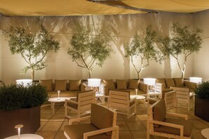 A modern lounge area with sofas and chairs, ambient lighting, and decorative trees. - Hotel Vilamari (Barcelona)
