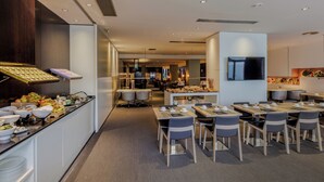 Un'area ristorazione moderna in hotel, con un buffet, posti a sedere e un televisore a parete.