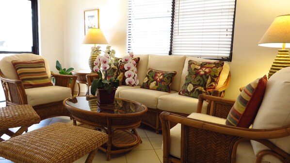 Un salón con muebles de mimbre, un sofá y una mesa baja con orquídeas.