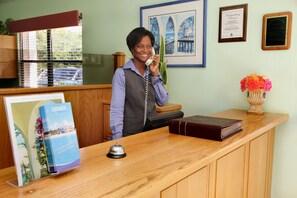 A reception desk with a wooden counter, a framed certificate on the wall, and a vase with flowers. - Carimar Beach Club (West End Village)