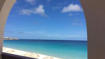 A view through an arched window of a beach with clear skies and calm sea.