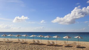 A beach with rows of sun loungers and umbrellas, a clear sky, and calm sea. - Carimar Beach Club (West End Village)
