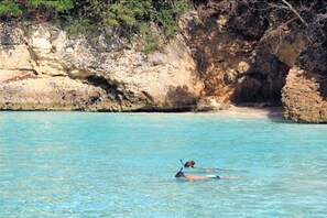 A coastal scene with clear turquoise water and rocky cliffs. - Carimar Beach Club (West End Village)