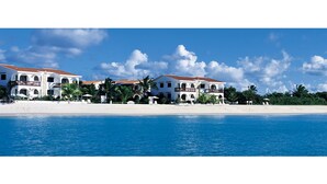 A beachfront hotel with multiple white buildings, palm trees, and a clear blue sky. - Carimar Beach Club (West End Village)