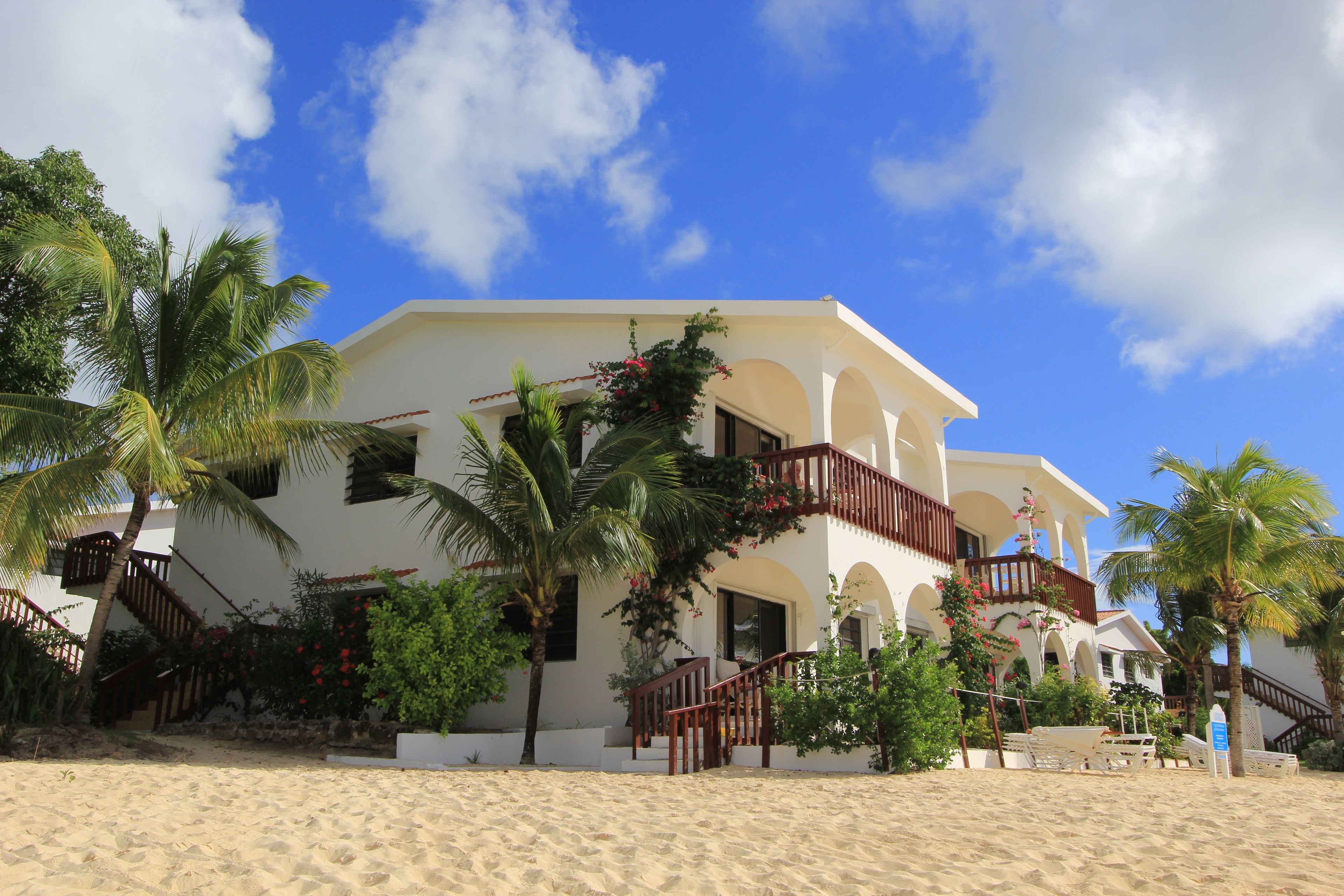 A beachfront property with a white building, multiple balconies, and palm trees.