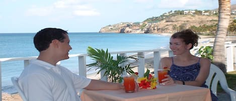 Una pareja sentada en una mesa al aire libre, con vista al océano y una colina de fondo.