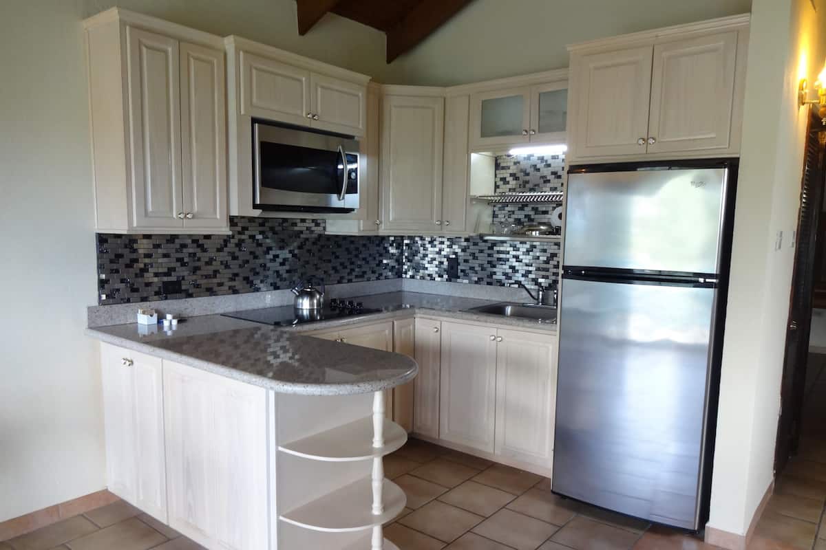 A kitchen with white cabinets, a stainless steel refrigerator, a microwave, and a tiled backsplash.