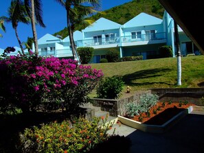 A resort with multiple blue buildings, a well-maintained garden with pink and red flowers, and a grassy hillside.