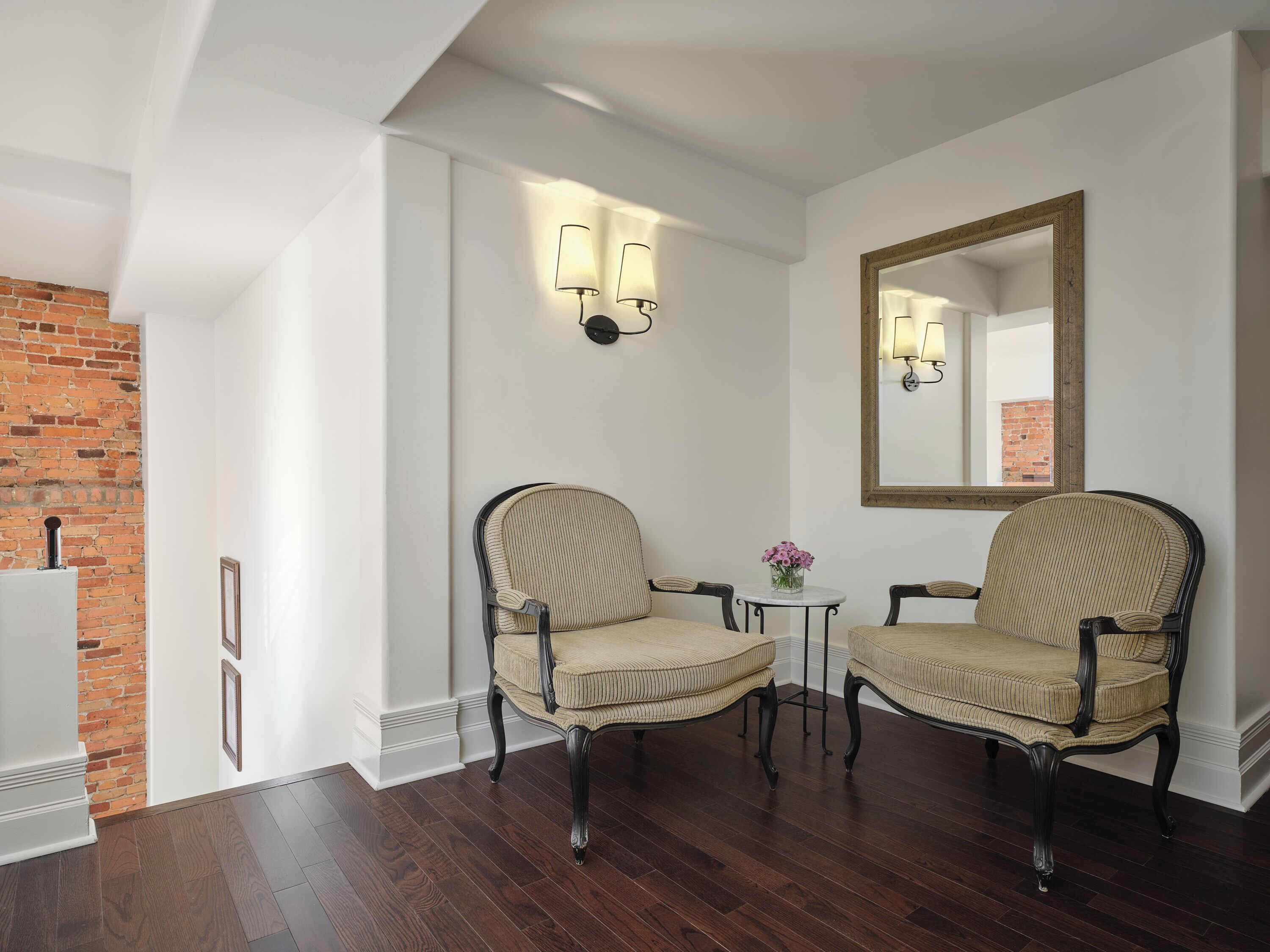Une pièce comprenant deux fauteuils rembourrés, une petite table ronde ornée d’un vase de fleurs et un grand miroir accroché au mur.