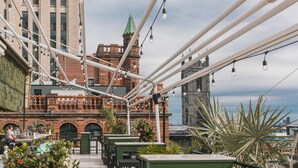 An outdoor seating area with tables and chairs, a brick building with a green roof, and a view of the cityscape. - Hotel Place d'Armes (Montreal)