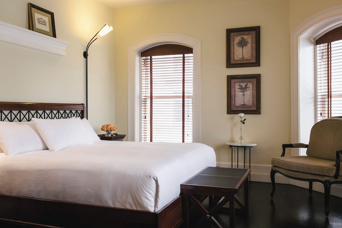 A neatly arranged bedroom with a large bed, a chair, a small table, and a lamp.
