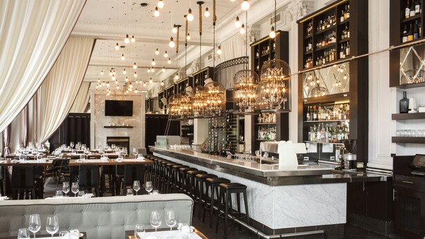 A bar area with a marble counter, multiple stools, and a variety of bottles and glasses. - Hotel Place d'Armes (Montreal)