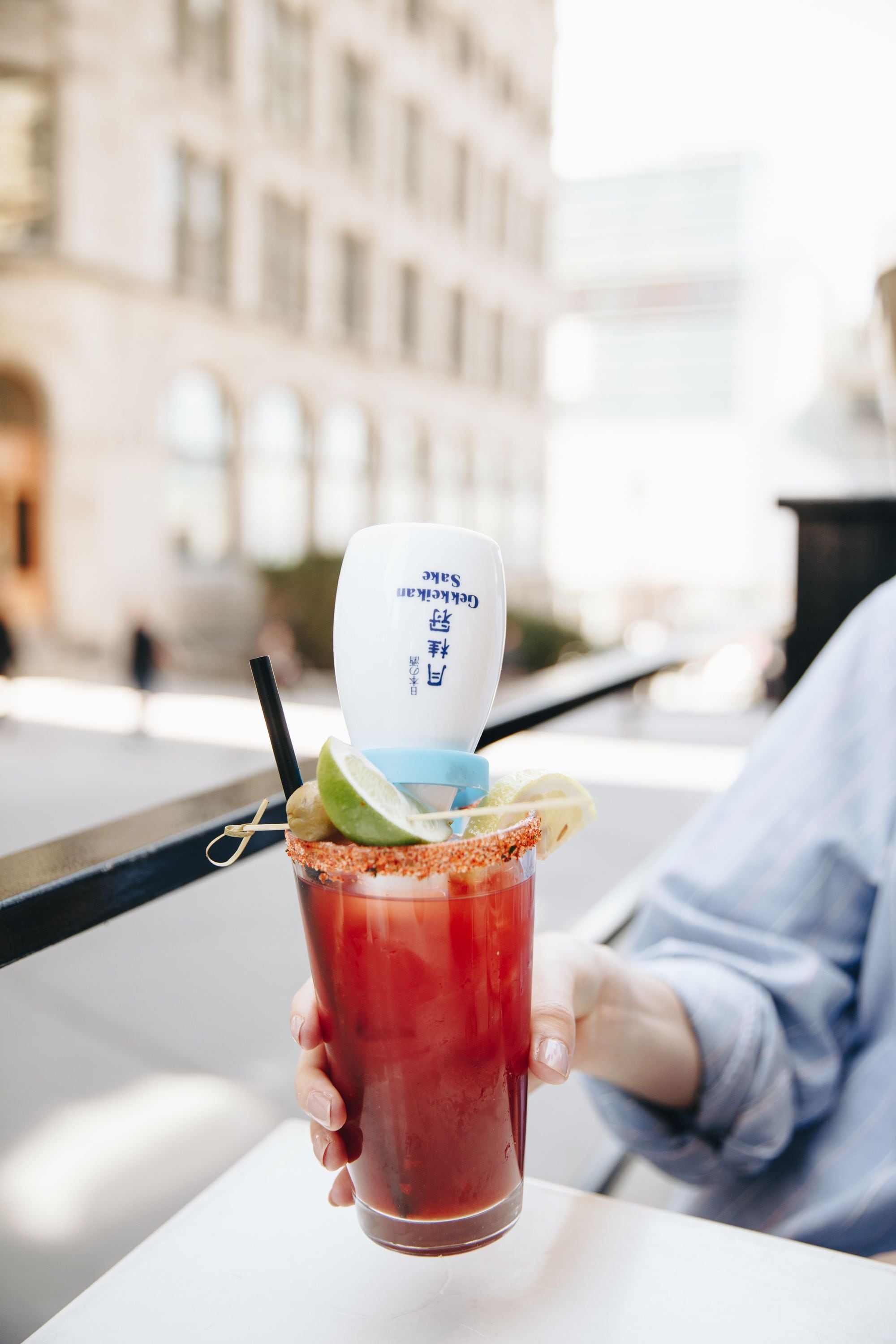 A person holding a red drink with a straw and a lime wedge, with a building in the background.