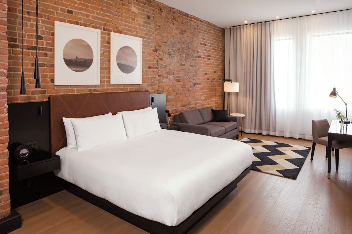 A hotel room with a large bed, a brick wall, a sofa, a desk, and a lamp.