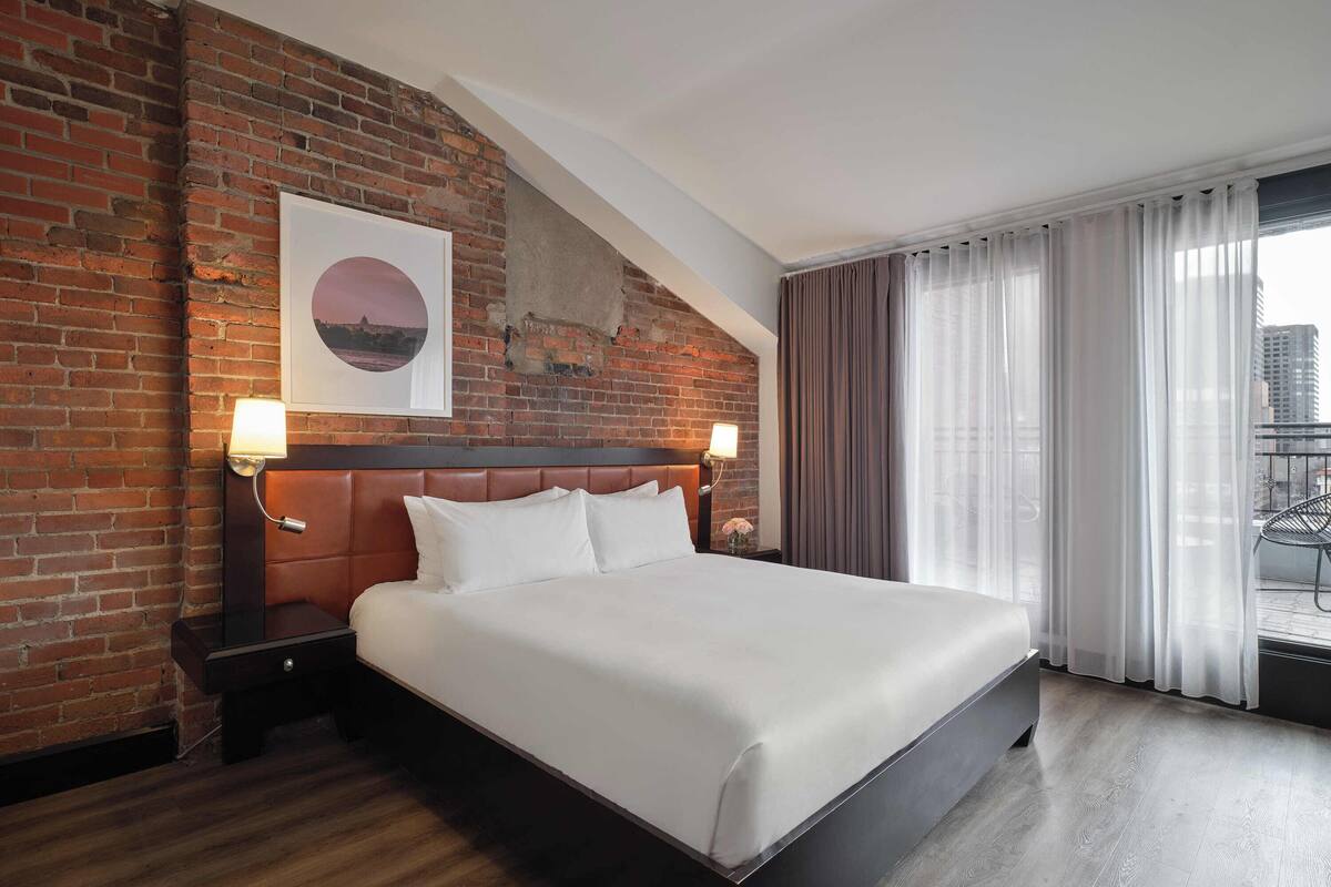 A hotel room with a large bed, brick wall, and a view of the city.