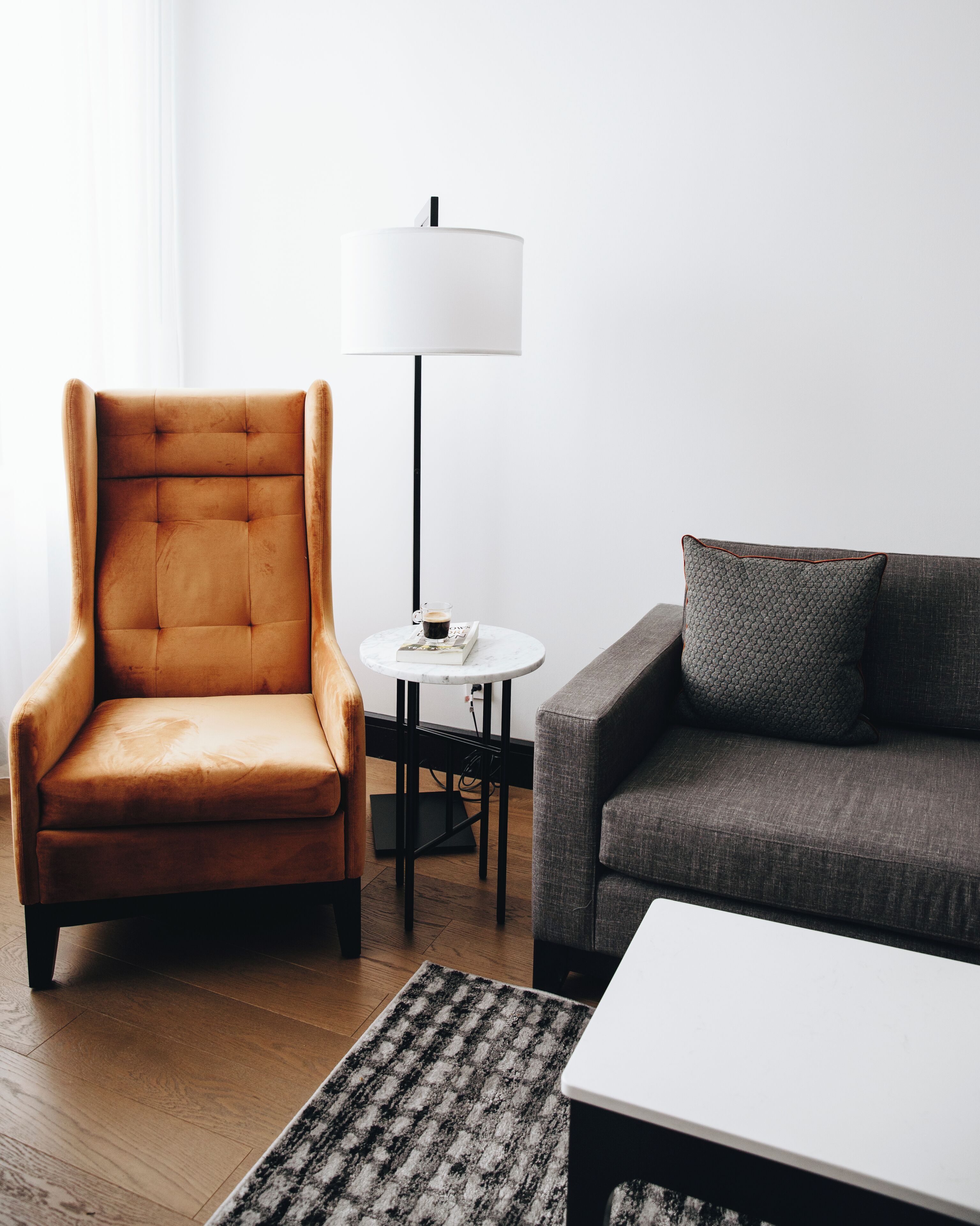 A modern living room with a brown armchair, a grey sofa, a white coffee table, and a floor lamp.